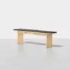 A modern wooden bench with thick rectangular legs and a black cushioned seat, set against a plain light background.
