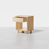 A minimalist wooden nightstand with an open square base, four short legs, and a single drawer that is partially pulled out. The nightstand is placed on a light gray floor against a plain white background.