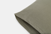 A close-up of an olive green pillow with a linen texture on a white background, showing the corner and part of the opening seam.