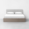 A modern bed with a light wood frame, a light gray upholstered headboard, and white bedding with two pillows, set against a plain white wall and floor.