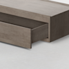 A close-up view of a wooden storage bed with a large drawer partially pulled out, revealing empty storage space inside, set on a light-colored floor.