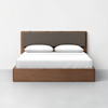 A modern wooden bed with a dark fabric headboard, two white pillows, and a white bedspread, set against a plain white wall and light gray floor.