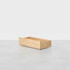 A light wood rectangular box with open top and sides sits on a smooth gray surface against a plain white background.