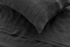 A close-up view of a neatly arranged dark gray linen pillow and matching bed sheet, showcasing the fabric’s soft, textured surface and natural creases.