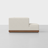 A modern, minimalist cream-colored sectional sofa with clean lines, low back, and a wooden base, viewed from the side against a plain white background.