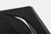 Close-up of a black, textured fabric cover with small white dots, partially unzipped to reveal a white inner layer and a gray border, set against a plain white background.