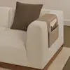 A modern beige sofa with a brown pillow and a tan leather armrest organizer holding a book, placed on a matching beige carpet.