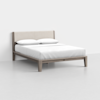 A modern wooden bed frame with a light beige upholstered headboard, neatly made with white bedding and two white pillows, set against a plain white wall and floor.