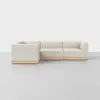 A modern, L-shaped sectional sofa with light beige upholstery and a wooden base, set against a plain, light gray background.