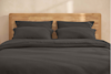 A neatly stacked set of dark gray bedding, including folded sheets and pillowcases, arranged on a light background.