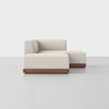 A modern, minimalist beige sectional sofa with clean lines and a low wood base, positioned in a bright, empty room with a light gray floor and a plain white background.