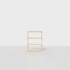 A simple, light wood three-shelf bookcase stands alone on a smooth, light gray surface against a plain white background.