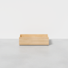 A single, empty, rectangular wooden drawer sits on a light gray floor against a plain white background.