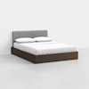 A modern bed with a gray upholstered headboard, white bedding, and a dark wood platform base, set in a minimalistic, white room.