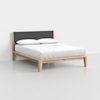 A modern wooden bed frame with a dark gray upholstered headboard, topped with a neatly made white mattress and two white pillows, set against a plain white wall and light gray floor.