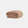 A neatly folded, light brown textured blanket is placed on a plain white background.