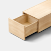 A light wood drawer, partially open, extends from a matching wooden cabinet against a plain light gray background. The drawer is empty and features clean, minimalist lines.
