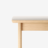 A close-up of a light wooden bench with a beige cushioned seat, shown against a plain white background.