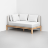A modern daybed with a light wood frame, light gray upholstered backrest, and white mattress, topped with three white pillows, positioned against a white wall on a light gray floor.