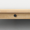 Close-up of a wooden bed frame with a visible round black screw in the center, attached to a light-colored wooden slat, against a light gray floor and white background.