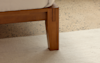 Close-up of a wooden bed frame leg with a white mattress on top, standing on a light-colored rug over a terrazzo floor.