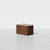 A modern wooden two-drawer dresser with a minimalist design, placed on a plain white floor against a white background.