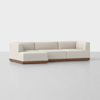 A modern sectional sofa with light beige upholstery and a low, wooden base, featuring a left-facing chaise lounge on a plain, light gray floor and background.
