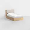 A single wooden bed with a padded beige headboard, white bedding, and a pillow, set against a plain white wall in a minimalistic room with a light gray floor.
