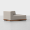 A modern, armless chaise lounge with light beige upholstery and a low, rectangular wooden base, set against a plain white background.