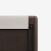 Close-up view of the corner of a dark wooden bed frame with a light beige upholstered headboard, showing the texture and sleek, modern design against a white background.