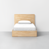 A wooden bed frame with a headboard and footboard, topped with a neatly made white bed and a single white pillow, set against a plain light-colored wall and floor.