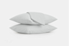 Two white pillows stacked on top of each other with a folded white sheet draped over the top pillow, all set against a plain white background.