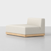 A modern armless chaise lounge with a low wooden base and light beige upholstered cushions, positioned on a smooth, light gray floor against a plain white background.