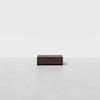 A minimalist scene with a single, dark rectangular wooden block centered on a smooth, light gray floor against a plain white background.