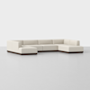 A modern, L-shaped sectional sofa with light beige upholstery and a dark wooden base, placed on a plain light gray floor against a white background.
