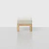 A minimalist ottoman with a light-colored cushioned seat and a natural wood frame, set against a plain light gray background.
