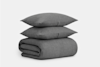 A neatly folded dark gray textured blanket with two matching pillows stacked on top, set against a plain white background.