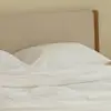 A neatly made bed with white linens and pillows stands in a modern, minimal bedroom. Shelves with decor items are in the background. A “Let’s get together” door hanger hangs on the open door.