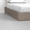 Close-up of a modern bed with a light wood platform frame, white bedding, and a white pillow, set on a smooth gray floor against a white wall.