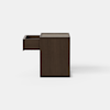A minimalist, square, dark brown wooden pedestal or box stands on a light gray floor against a plain white background.