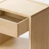 A minimalist wooden cabinet viewed from the side, with a single drawer partially open, standing on a smooth, light-colored floor against a plain white background.