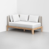 A modern daybed with a light wood frame, beige upholstered backrest, and seat cushions. Three white pillows are arranged against the back, and the daybed sits in a minimalist, white-walled room.