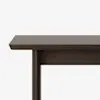 A close-up view of the corner of a dark brown wooden table against a plain white background, showing the tabletop, one leg, and part of the table’s side panel.