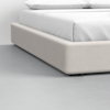 Close-up view of a modern bed with a light beige upholstered frame and white bedding, set on a smooth, light gray floor.