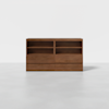 A low, rectangular wooden shelving unit with a natural finish, featuring two open shelves on each side and two drawers beneath each set of shelves, set against a plain white background.