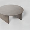 A round wooden coffee table with a smooth surface and sturdy, solid legs set against a plain, light-colored background.