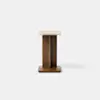A modern side table with a square beige stone top, a wooden base featuring two intersecting vertical panels, and a square wooden platform at the bottom, all set against a plain light background.