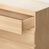 A close-up of a light wood dresser with one drawer partially open, showing simple, modern design and smooth, natural woodgrain texture.