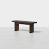 A minimalist wooden bench with a dark brown finish and a black cushioned seat, positioned on a light-colored floor against a plain white background.