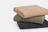 A neatly folded stack of three quilts in beige, olive green, and dark gray colors, arranged on a white background.